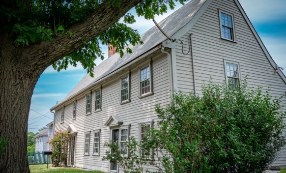 An exterior photo of pierce house showing the side and front of the house. There is a tree and bushes visible.