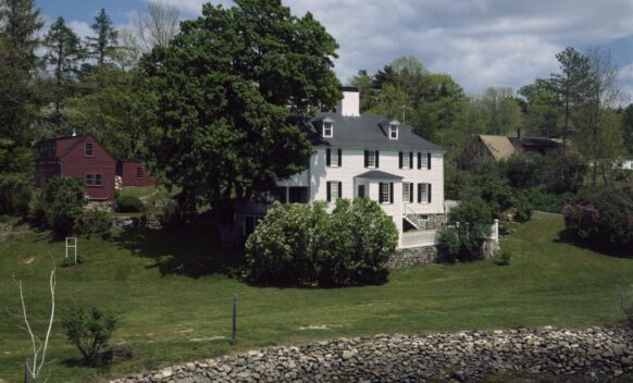 An aerial photo of the back exterior of Sayward-Wheeler House in York Harbor, Maine. A rocky shore and water are visible.