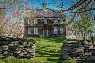 A photo of the front of Watson Farm. Two rock walls with an opening in the middle allow access to the front of the house.