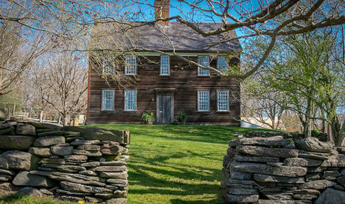 A photo of the front of Watson Farm. Two rock walls with an opening in the middle allow access to the front of the house.