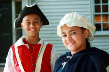 A photo of two younger people in colonial costume looking toward the camera and smiling.