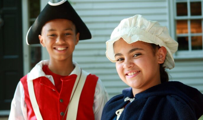A photo of two younger people in colonial costume looking toward the camera and smiling.