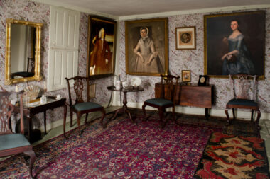 A photo of an opulent room with bright carpeting and portraits hanging on the wall.
