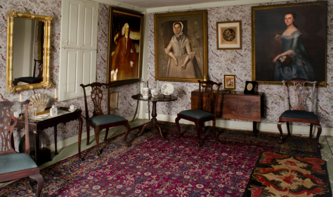 A photo of an opulent room with bright carpeting and portraits hanging on the wall.