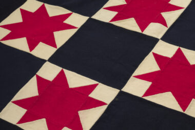 A photo of a quilt with black and white checkered squares. Filling the white squares are red, 8-pointed stars.