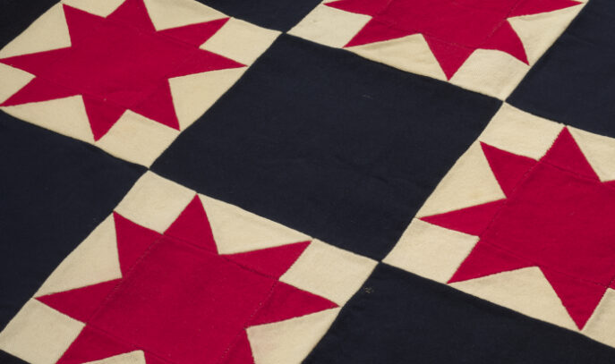 A photo of a quilt with black and white checkered squares. Filling the white squares are red, 8-pointed stars.