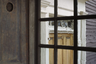 A photo of old windows overlooking an exterior door. The large wooden shutters are open.