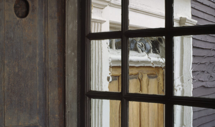 A photo of old windows overlooking an exterior door. The large wooden shutters are open.