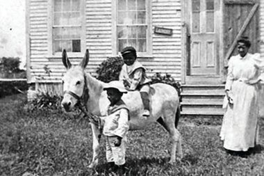 The book cover for A Peaceful Patch of Earth. It shows a picture of a family in front of a house with a boy riding a small donkey.