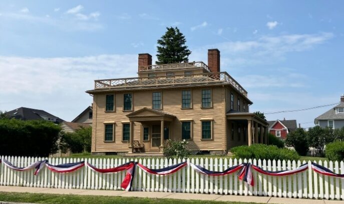 An exterior photo of Quincy House. The white picket fence out front is visible with red, white, and blue bunting.